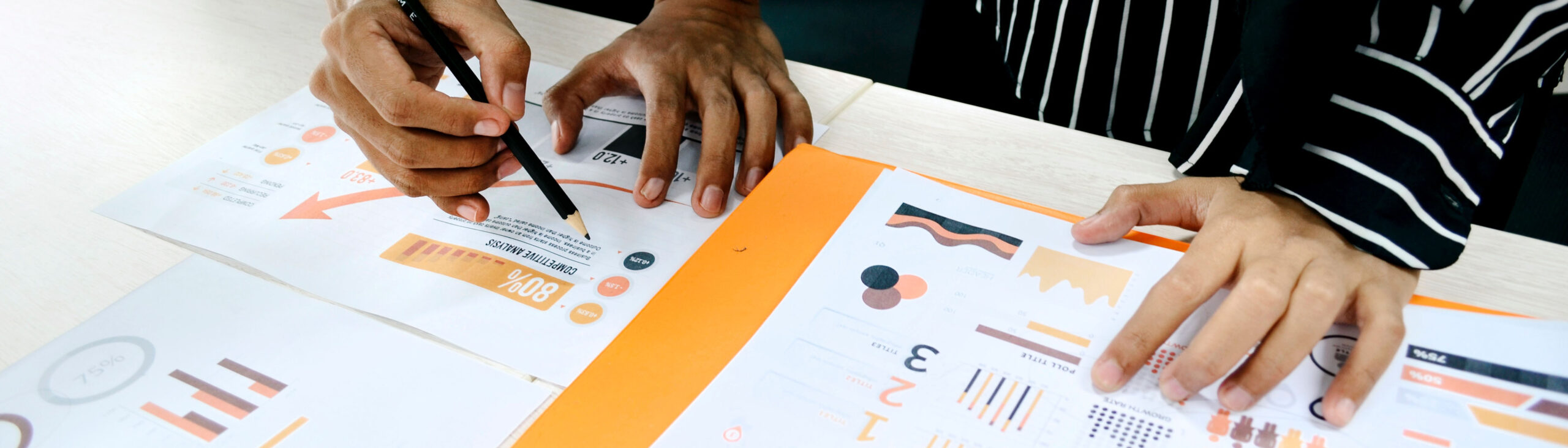 one person holding a pencil marking some printed graphs on paper, alongside another person.